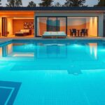 Modern családi medence esti fényekkel egy elegáns ház előtt.