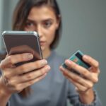 Nő bankkártyáját tartja a kezében, telefonját használva.