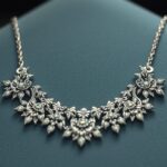 Díszes ezüst nyaklánc virágmintával, kék háttérrel.