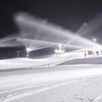 Hóágyúzás a sípályán éjszaka, havas táj és világító berendezések.