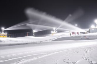 Hóágyúzás a sípályán éjszaka, havas táj és világító berendezések.