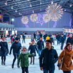 Családok és barátok korcsolyáznak a jégpályán, ünnepi díszekkel.