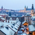 Téli táj Prágában, hóval borított tetők és történelmi látványosságok.